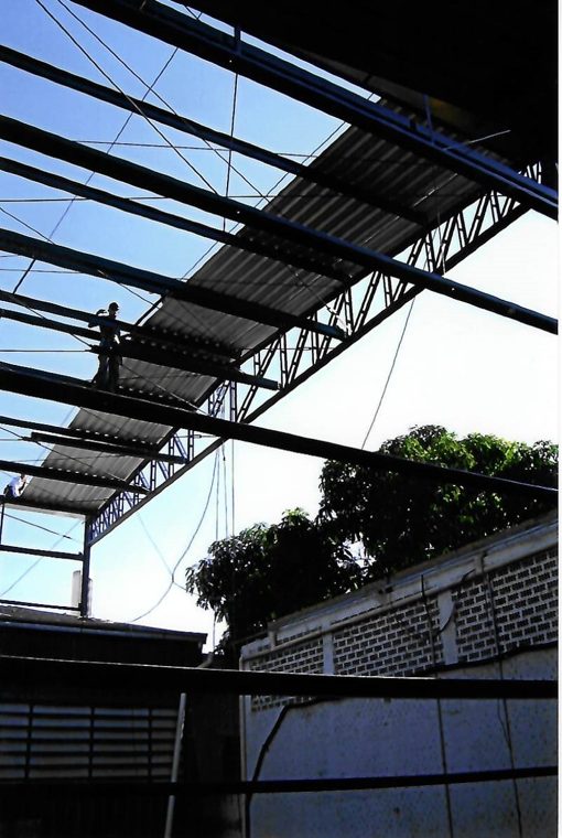 Estrutura metálica de tesoura sendo montada contra o céu, com operário no alto, por volta de 2010